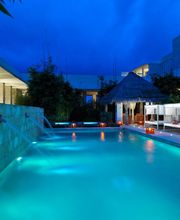 Piscina iluminada de noche, rodeada de palapas y tumbonas, bajo un cielo azul profundo.
