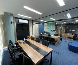 Escritório moderno com mesas de madeira, cadeiras pretas e divisórias de vidro.