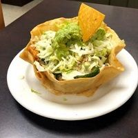 Taco salad in a crispy shell with guacamole, shredded cheese, and a tortilla chip garnish.