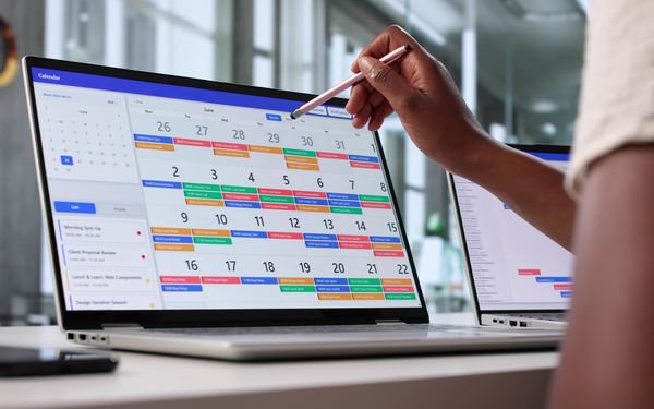 Person plant Termine und Urlaubszeiten in einem digitalen Kalender auf dem Laptop.