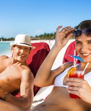 Pareja relajándose en la playa con bebidas tropicales, disfrutando del sol y el mar.