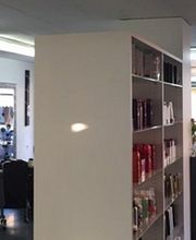 Friseursalon mit Kunden, Regalen mit Produkten und großen Werbeplakaten an den Fenstern.