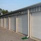 Row of closed storage unit doors with a metal roof and gravel pathway.