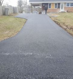 Newly paved asphalt driveway leading to a house with a single person in the distance.