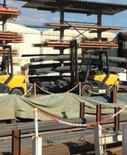 Carrelli elevatori gialli in un cantiere con materiali edili e coperture.