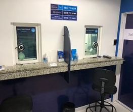 Balcão de atendimento com duas janelas, cadeira e placas azuis na parede.