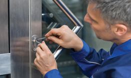 Hombre abriendo una cerradura con una herramienta en una puerta de vidrio y metal.