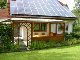 Haus mit Solarpanels, überdachter Terrasse und Garten im Vordergrund.