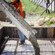Worker pouring concrete into a rebar frame at a construction site.
