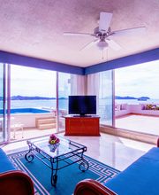 Sala con sofás azules, mesa de centro y vista al mar desde ventanales y terraza.