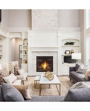 Sala elegante con chimenea, sofá gris, sillas beige y ventanales grandes.