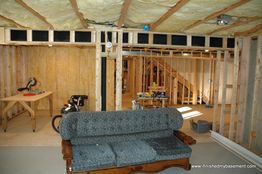 Unfinished basement with exposed wooden framing, a couch, and a workbench in the background.
