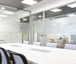 Sala de reuniones moderna con mesa blanca y sillas negras, paredes de vidrio y luz natural.