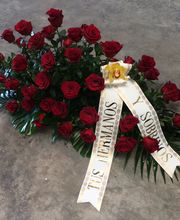Arreglo de rosas rojas con cinta de condolencias blanca sobre suelo gris.