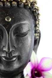 Buddha-Statue mit geschlossenen Augen und lila Orchidee im Vordergrund.