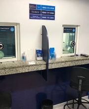 Balcão de atendimento com duas janelas, cadeira e placas azuis na parede.