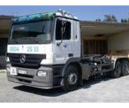 LKW mit weißer Kabine und blau-grünen Akzenten, geparkt auf einem Hof vor einer Halle.