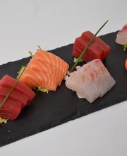 Surtido de sashimi de salmón, atún y pescado blanco sobre tabla negra.