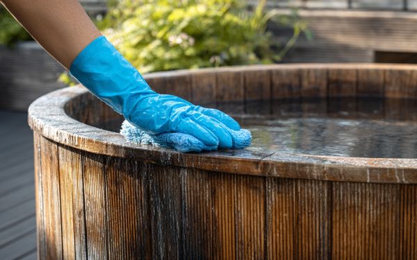 Mit Wasser gefülltes, verwittertes Badefass wird mit einem Reinigungstuch von Hand gesäubert.