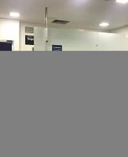 Saguão de um banco com portas de vidro e placas de sinalização. Luzes de teto visíveis.