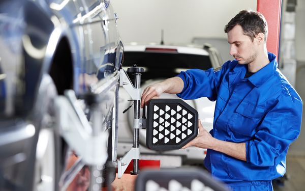 Mechatroniker arbeitet an der Achsenvermessung eines PKWs in seiner Werkstatt.