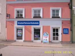 Rosa Gebäude mit Schildern "DruckerPatronenTankstelle", "Toner" und "Tinte" über dem Eingang.