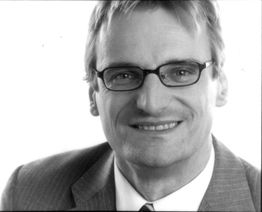 Porträt eines Mannes mit Brille und Anzug, lächelnd, Schwarz-Weiß-Foto.