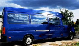 Blauer Van unter bewölktem Himmel, parkend auf einer Straße.