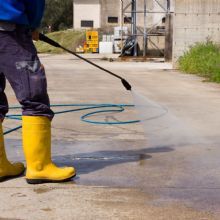 Person using a pressure washer on concrete, wearing yellow boots.