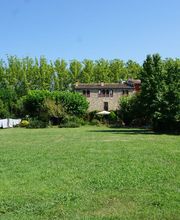 Extensa pradera verde con árboles y una casa de piedra al fondo bajo un cielo azul.