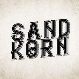 Schwarz-weißer Schriftzug "SANDKORN" auf einem beigen Hintergrund mit dekorativem Stil.