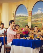 Grupo de personas brindando en un restaurante con decoración de murales de paisajes.