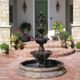 A stone fountain in front of a house with brick steps and potted plants near the entrance.