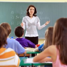 Teacher instructing attentive students in a classroom with math problems on the chalkboard.