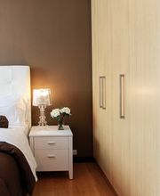 Dormitorio moderno con cama blanca, lámpara sobre mesita, y armario de madera clara.