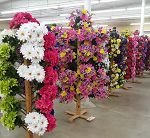 Artificial flower stands display colorful blooms in rows inside a brightly lit store.