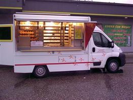 Foodtruck mit Beleuchtung und geöffneter Theke, geparkt vor einem Gebäude.