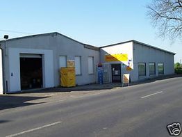 Graues Gebäude mit gelbem Schild neben einer Straße bei klarem Himmel.