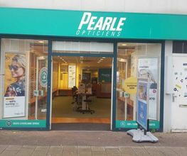 Winkelgevel van Pearle Opticiens met posters en een groene luifel.