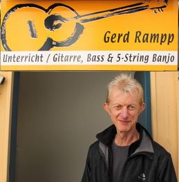 Mann steht unter einem Schild für Gitarrenunterricht von Gerd Rampp.