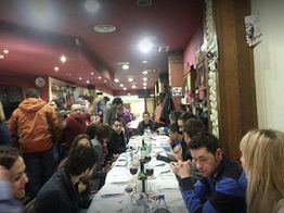 Personas cenando en un restaurante, sentadas a una mesa larga con vino y charlando animadamente.