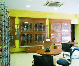 Tienda de óptica con estantes de gafas y sillas para atención al cliente.