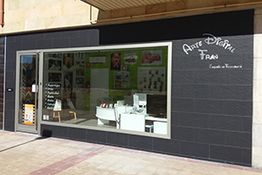 Fachada de una tienda de arte digital con vitrinas y carteles en la entrada.