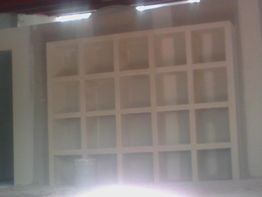 Estantería blanca en una habitación, con varios compartimentos cuadrados vacíos y una cubeta.