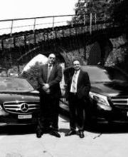 Zwei Männer stehen vor zwei Mercedes-Autos unter einer Brücke.