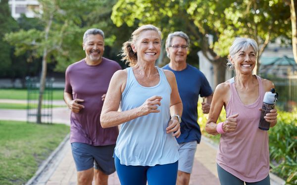 Vier ältere Erwachsene joggen gemeinsam gut gelaunt auf einem Weg im Park.