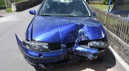 Blauwe auto met zware schade aan de voorkant, geparkeerd op een straat.