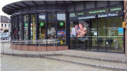 Geschäft mit Glasfassade und Werbung, "delmediatec Kabel Point", grünem und blauem Schriftzug.