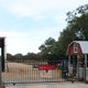 Entrance gate to a farm with a barn and trees in the background.