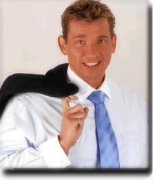 Mann in Hemd und Krawatte hält seine Jacke über die Schulter und lächelt in die Kamera.